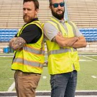 Jake Mallekoote and Matt DeRuiter standing back to back with their arms crossed, wearing construction vests and looking seriously into the camera